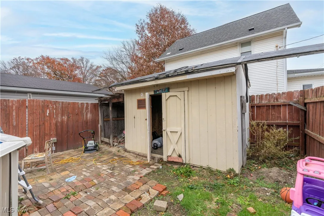 Rear view of property with a fenced backyard, roof with shingles, a shed, and a patio area
