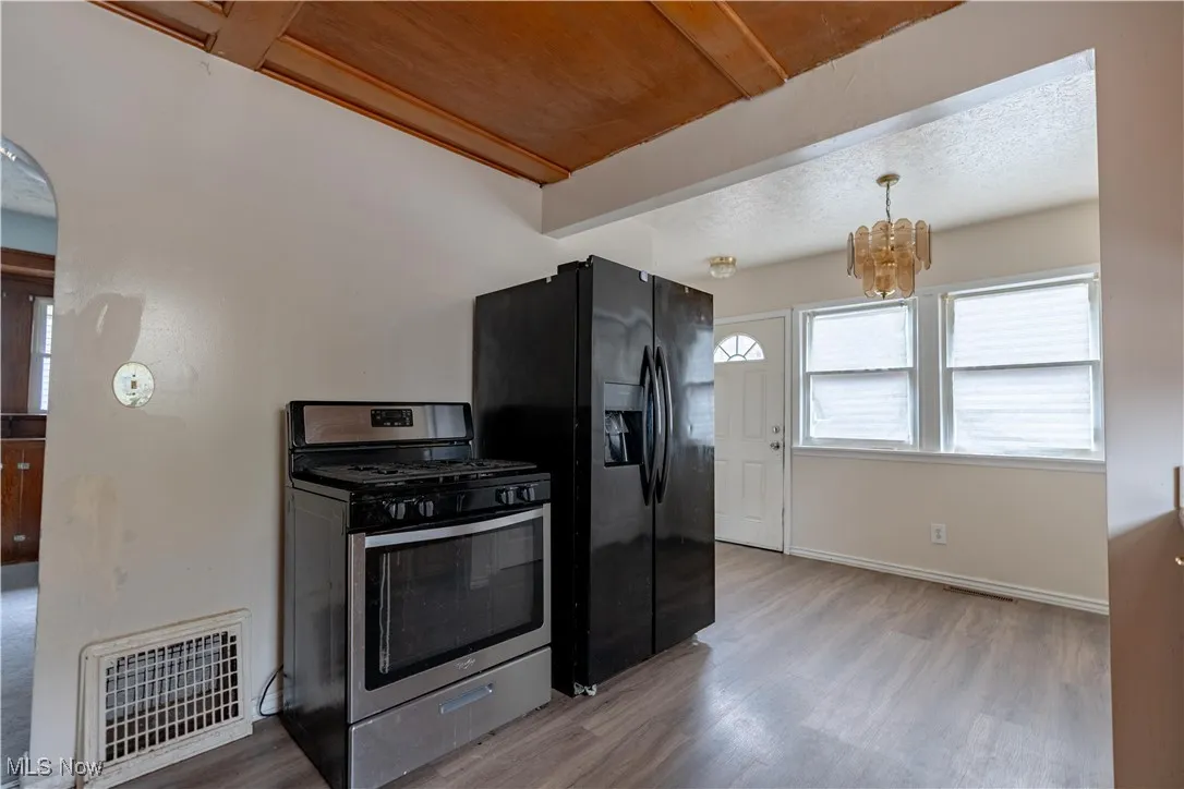 Kitchen featuring stainless steel range with gas cooktop, light wood-style flooring, fridge with ice dispenser, a chandelier, and decorative light fixtures