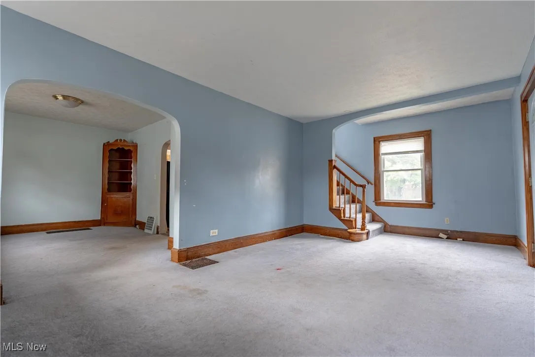 Carpeted spare room with stairs and arched walkways
