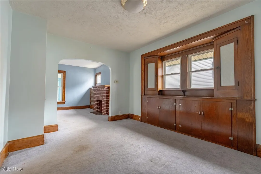 Empty room with light colored carpet, a textured ceiling, and arched walkways