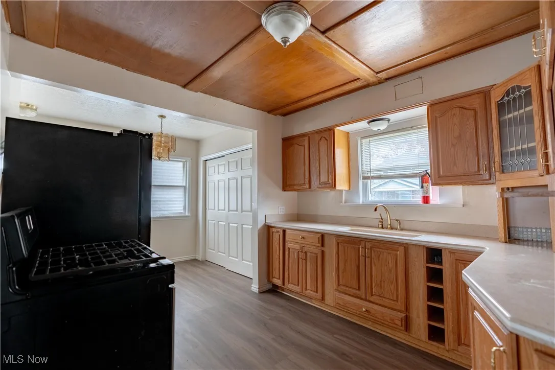 Kitchen featuring black appliances, light wood finished floors, glass insert cabinets, light countertops, and hanging light fixtures