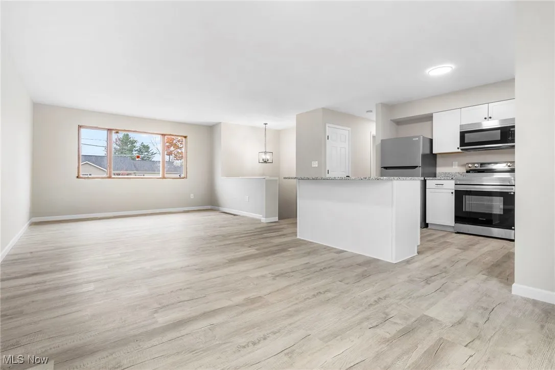 Kitchen with stainless steel appliances, a center island, light wood finished floors, white cabinets, and open floor plan
