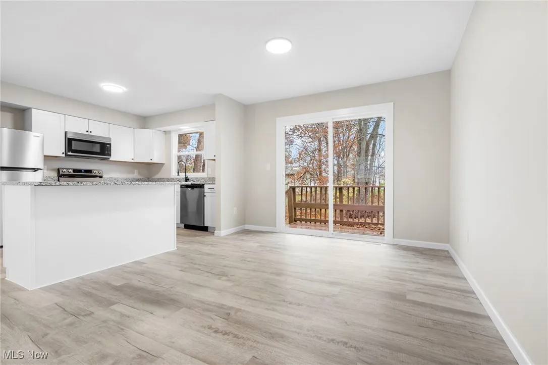 Kitchen featuring appliances with stainless steel finishes, white cabinets, light wood finished floors, a kitchen island, and light stone countertops