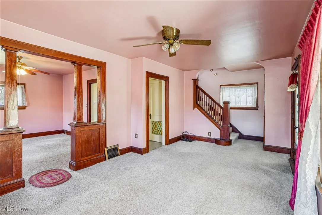Living room looking into the dining room with ceiling fan / light, stairway to second floor and carpet flooring.