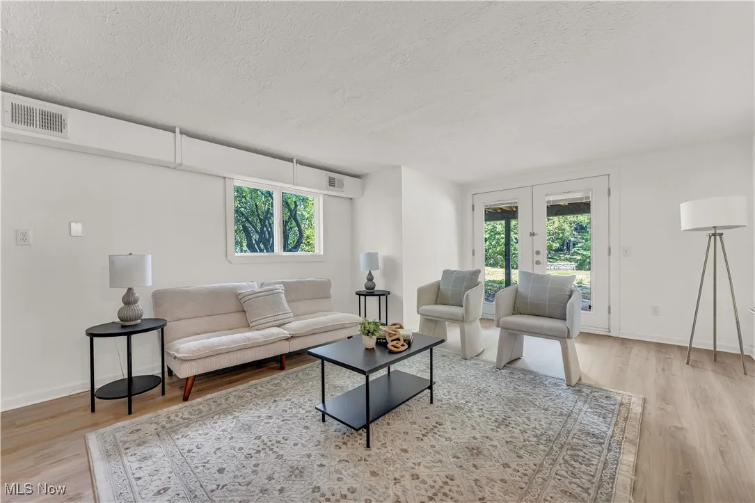 Living area featuring light wood-style floors, a textured ceiling, french doors, and healthy amount of natural light