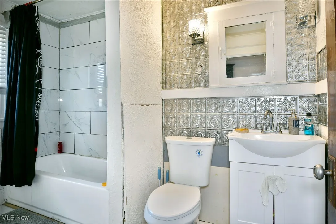 Full bathroom featuring vanity, shower / bath combo with shower curtain, and a textured wall
