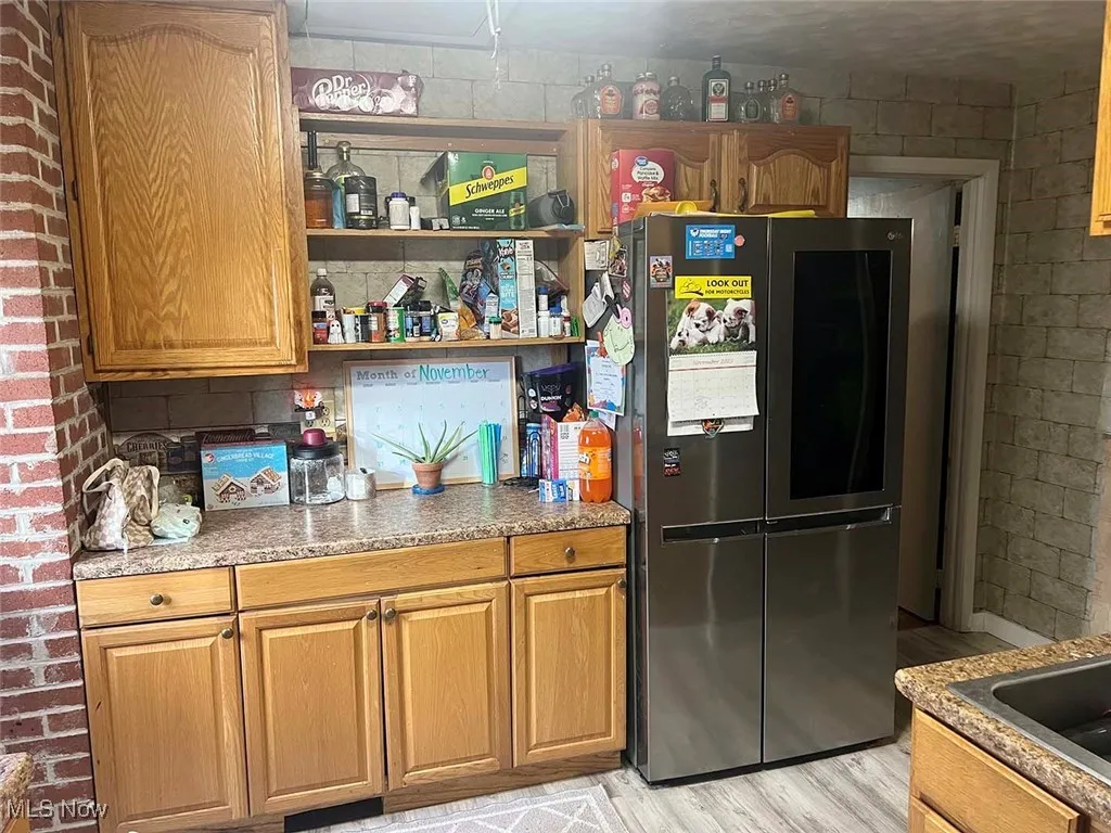 Kitchen featuring smart refrigerator, brown cabinetry, light wood-type flooring, concrete block wall, and open shelves