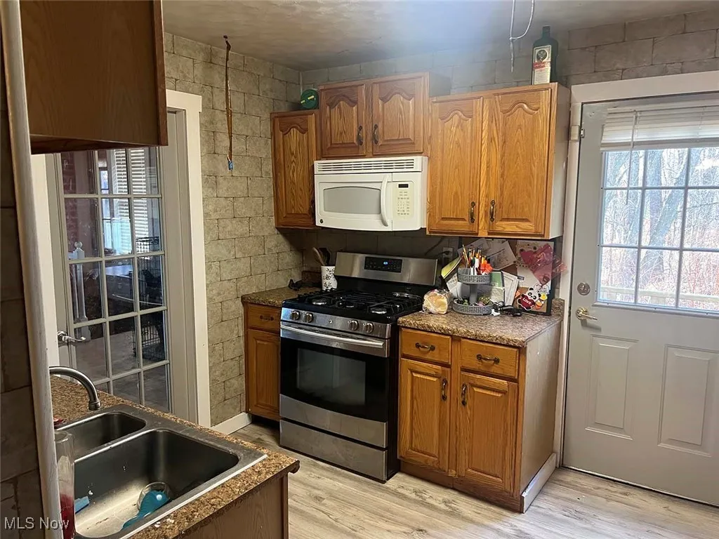 Kitchen with gas stove, brown cabinetry, white microwave, and light wood-style floors