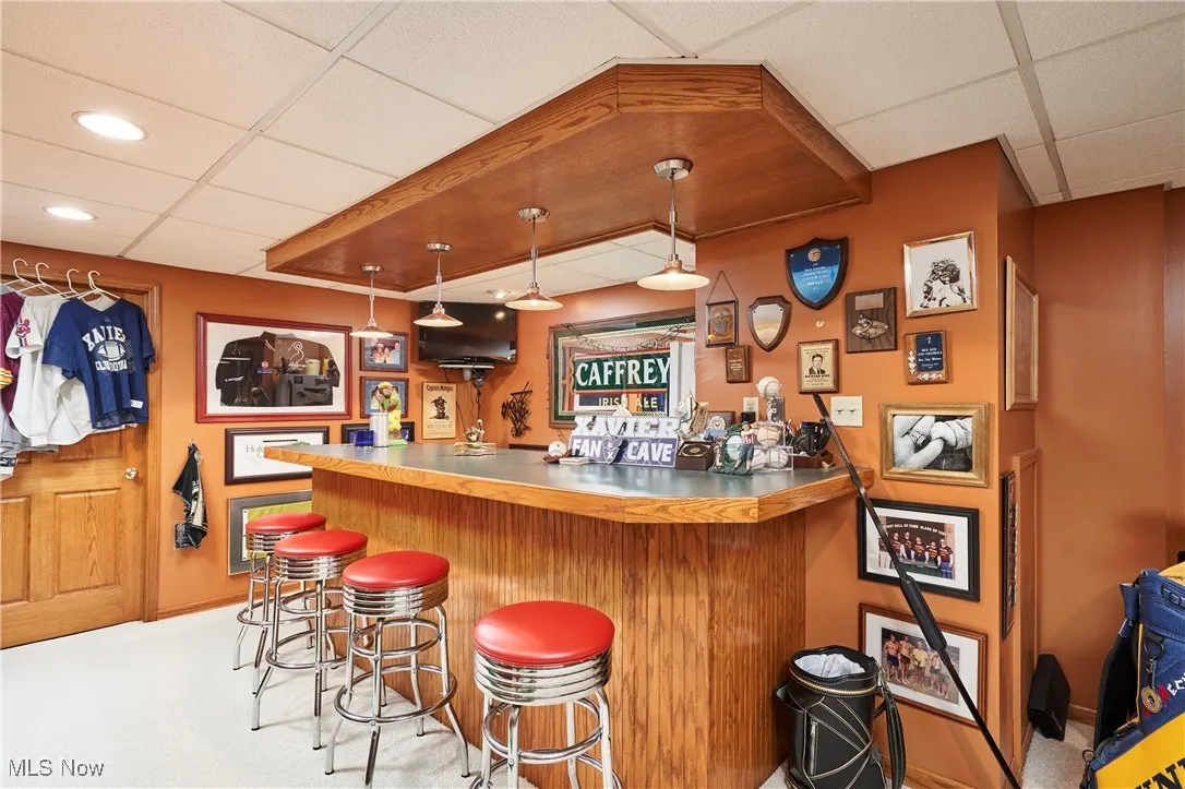 Indoor bar with a paneled ceiling, hanging light fixtures, light carpet, and brown cabinets