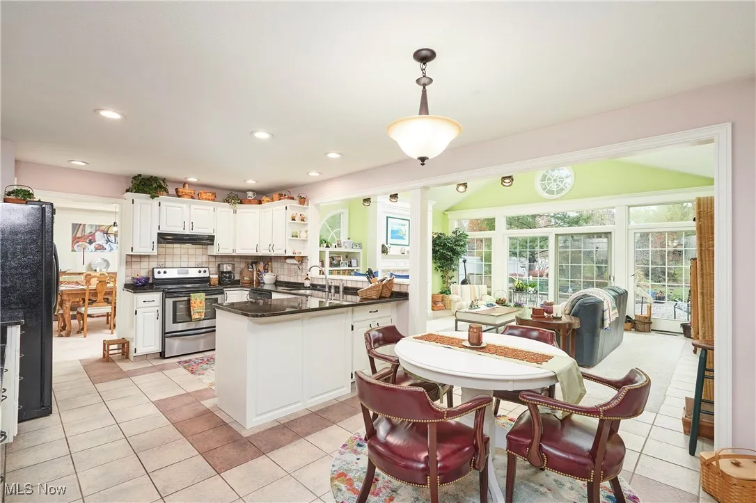 Kitchen featuring a peninsula, white cabinetry, decorative backsplash, stainless steel range with electric stovetop, and freestanding refrigerator