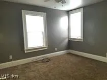 Empty room featuring dark colored carpet and a ceiling fan