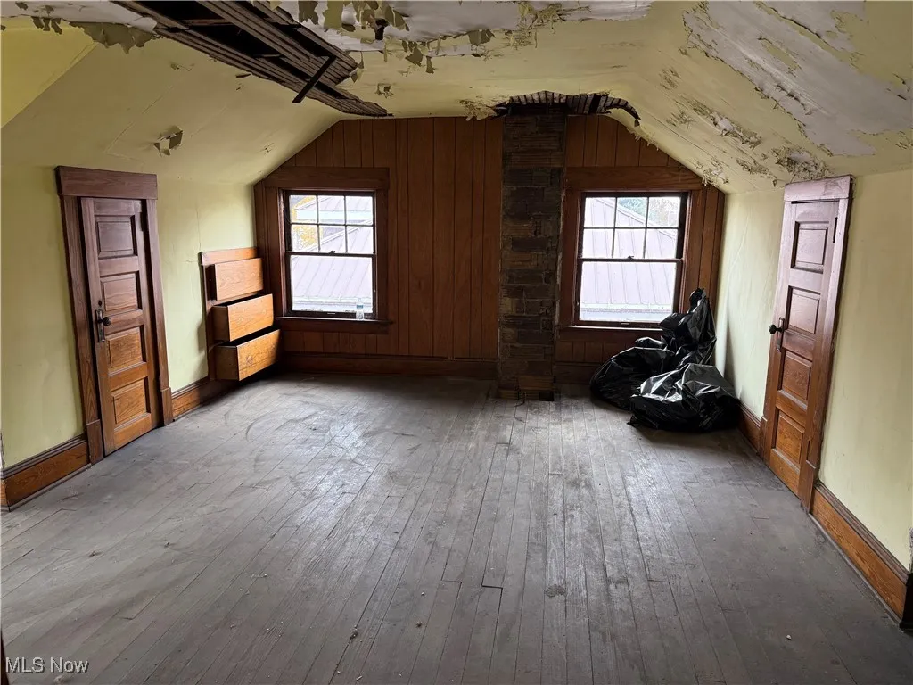 Bonus room with hardwood / wood-style floors, wood walls, lofted ceiling, and plenty of natural light
