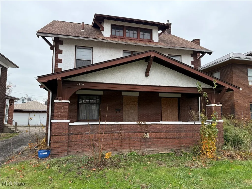 American foursquare style home featuring covered porch, stucco siding, brick siding, and roof with shingles