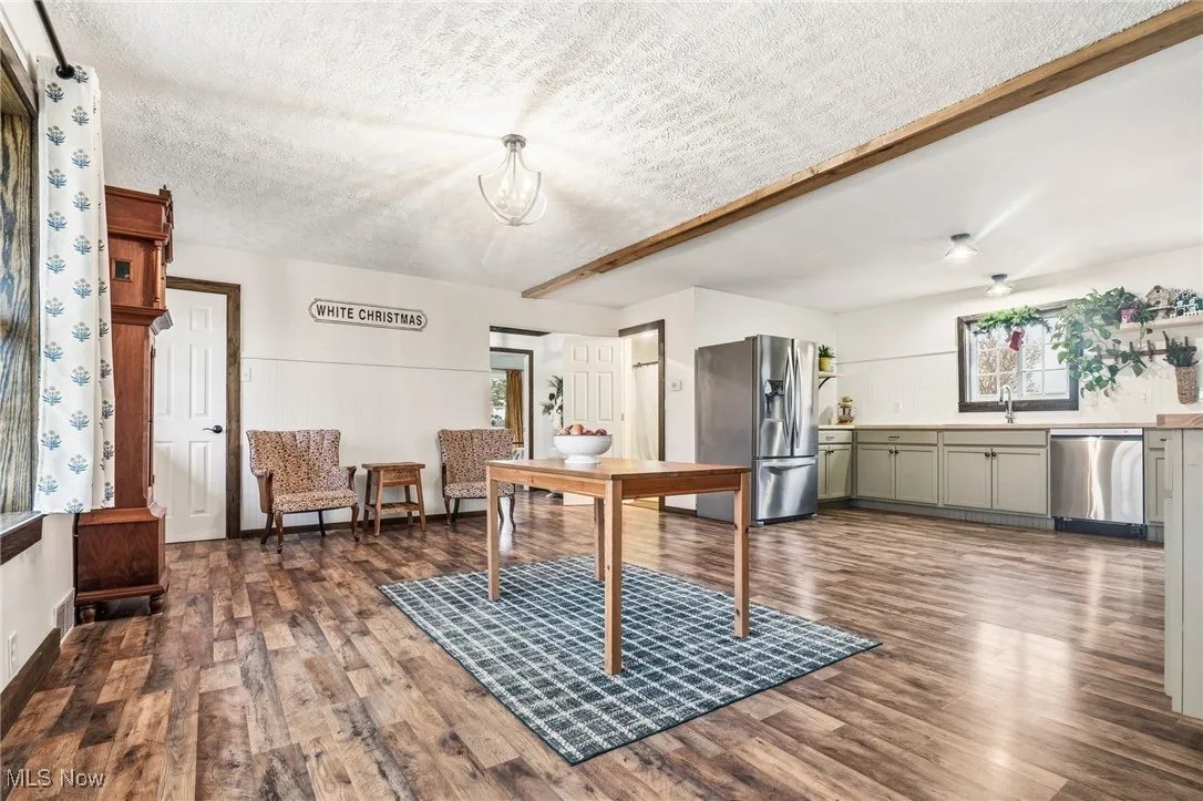 Dining room with dark wood-style flooring, beam ceiling, and a textured ceiling