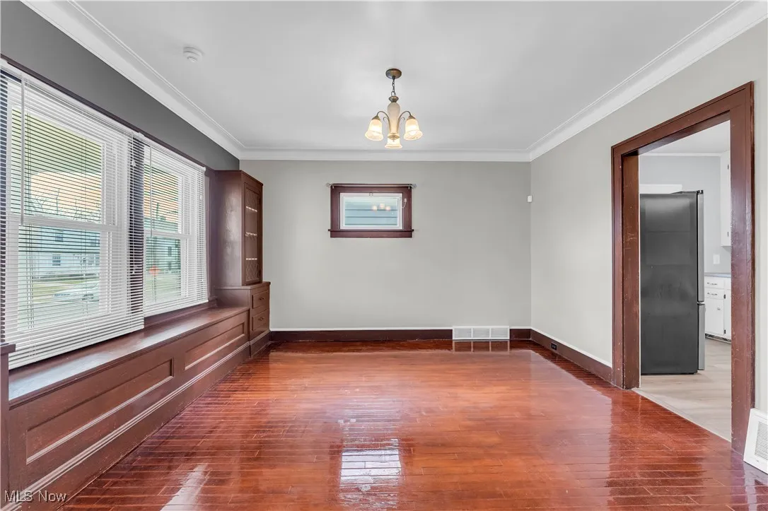 Unfurnished room with a chandelier, ornamental molding, and dark wood-style floors