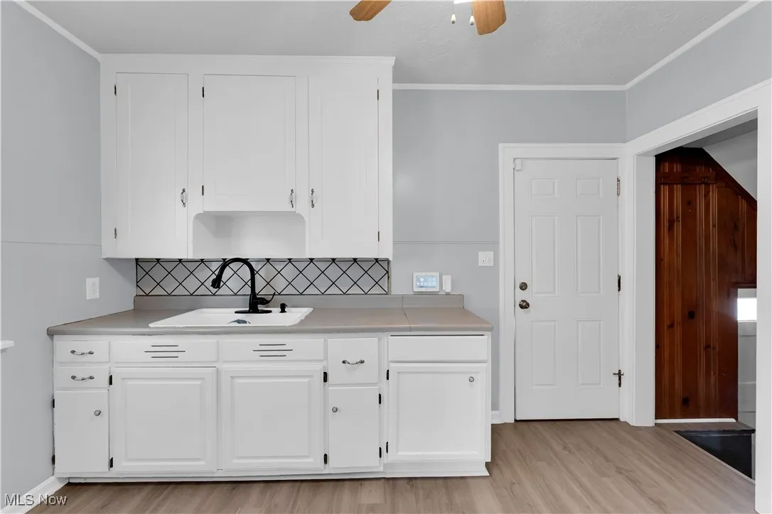 Kitchen featuring white cabinets, light wood-type flooring, light countertops, backsplash, and ceiling fan