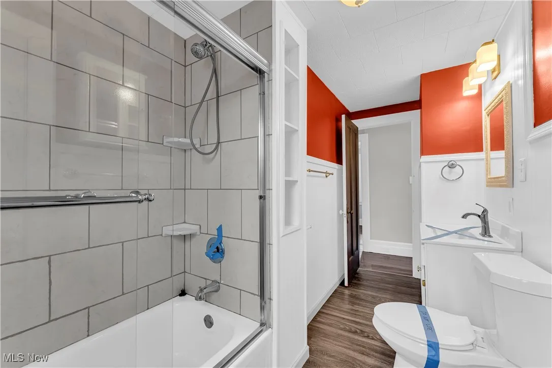Bathroom with enclosed tub / shower combo and dark wood-type flooring