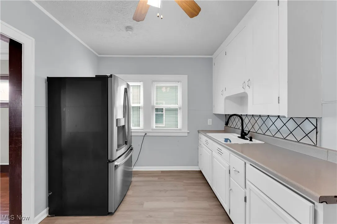 Kitchen with stainless steel fridge, light wood-type flooring, white cabinetry, light countertops, and a textured ceiling