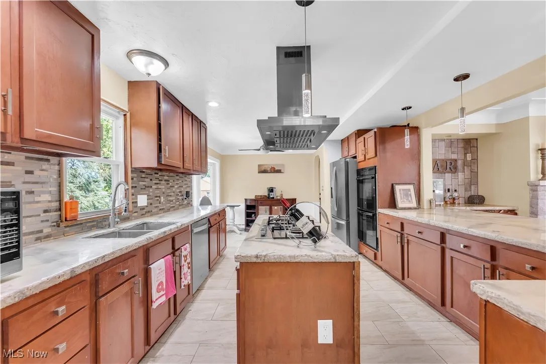Kitchen with backsplash, brown cabinetry, light stone countertops, pendant lighting, and recessed lighting