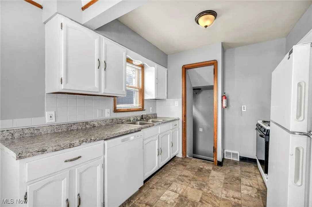 Kitchen featuring backsplash, white appliances, white cabinets, and stone finish flooring