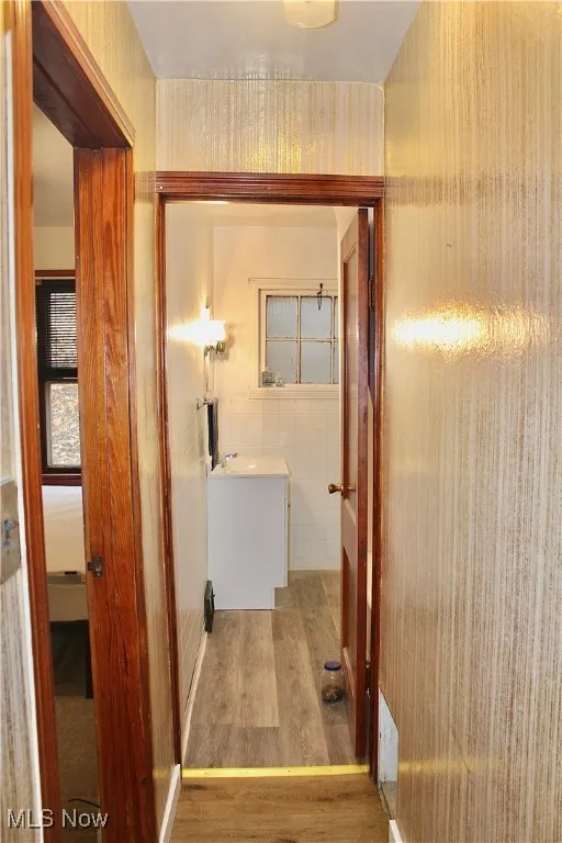 Corridor with light wood-type flooring, tile walls, and wallpapered walls