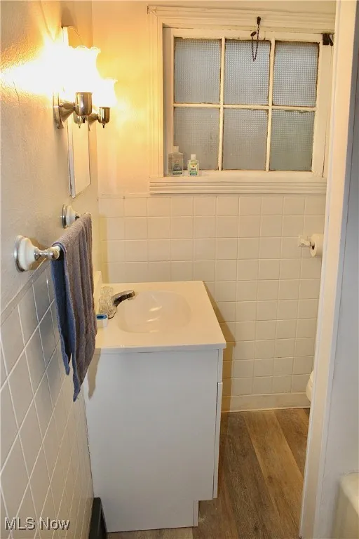 Bathroom with tile walls, dark wood-style floors, vanity, and wainscoting
