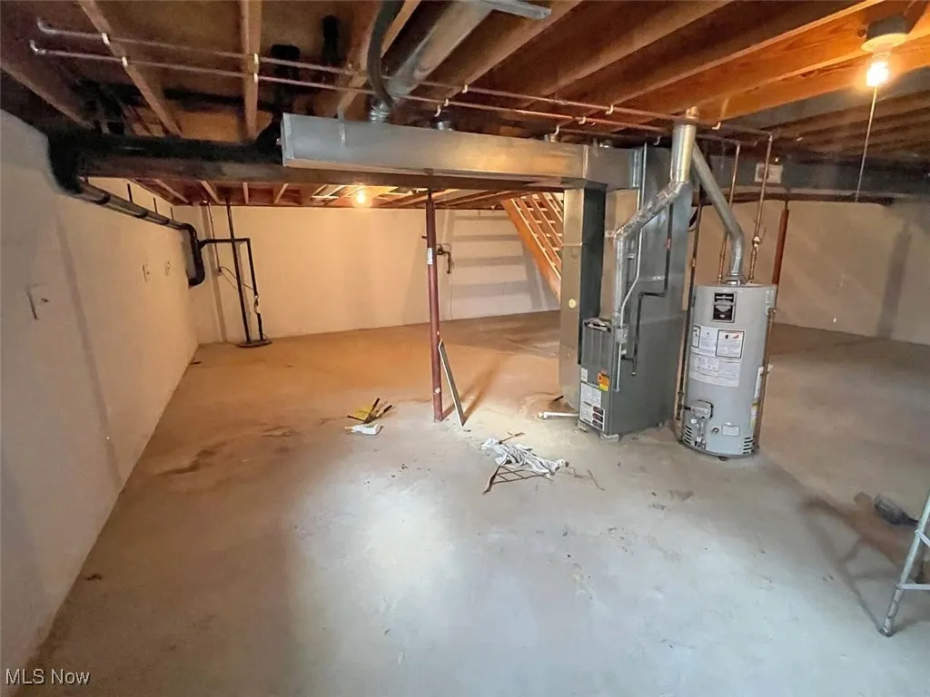 Unfinished basement with stairway, gas water heater, and heating unit