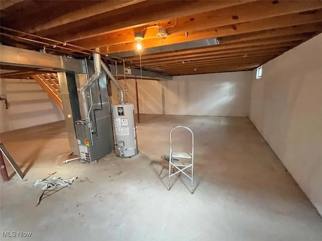 Unfinished below grade area featuring stairs, gas water heater, and heating unit
