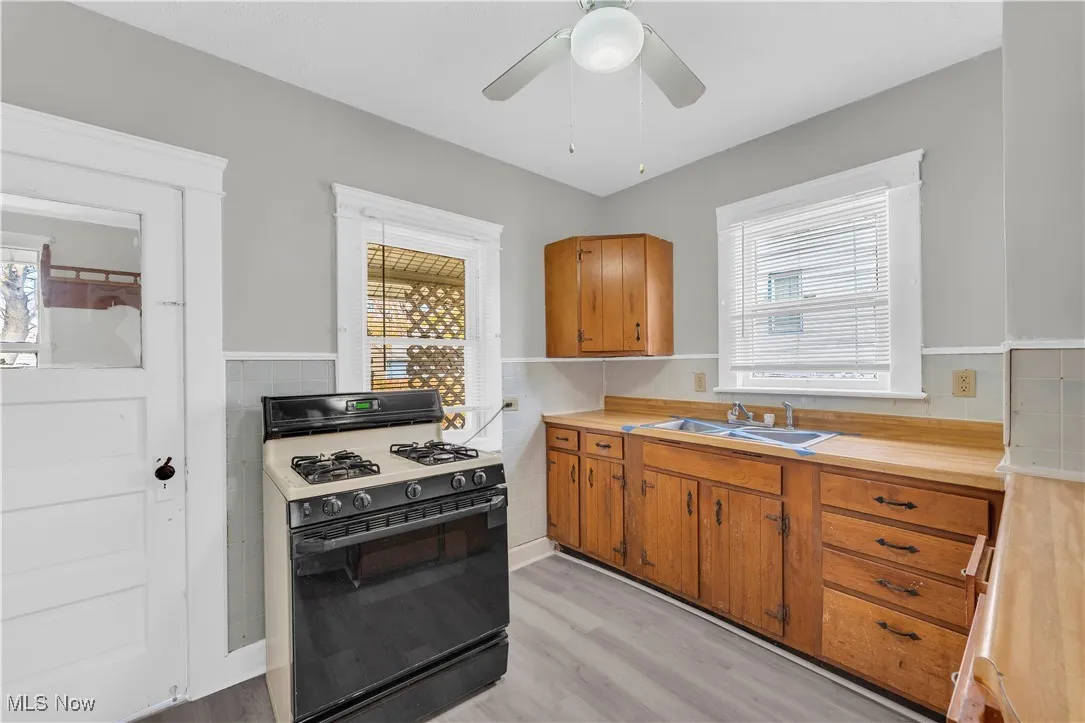 Kitchen featuring gas stove, light countertops, brown cabinetry, light wood-type flooring, and tile walls