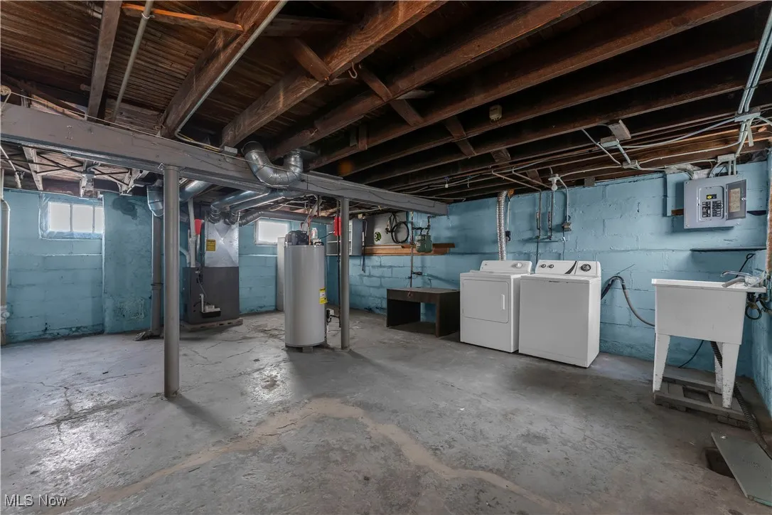 Below grade area with water heater, electric panel, heating unit, and washing machine and clothes dryer