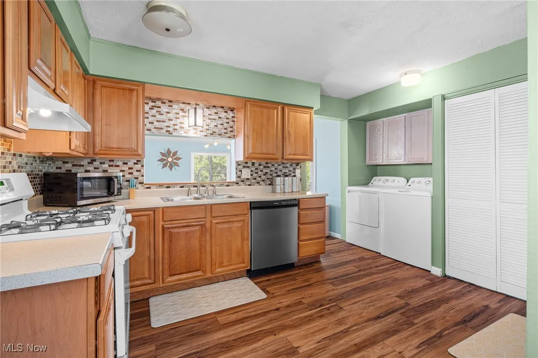 Kitchen featuring appliances with stainless steel finishes, light countertops, dark wood finished floors, washer and dryer, and under cabinet range hood