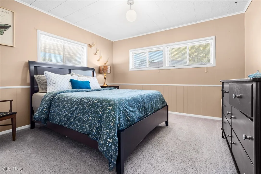 Bedroom with wainscoting, ornamental molding, wooden walls, and carpet