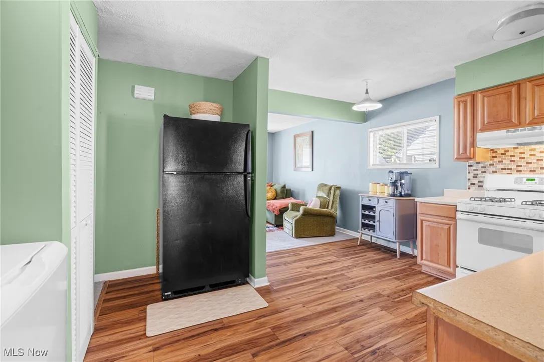 Kitchen with white gas range, freestanding refrigerator, light wood finished floors, light countertops, and under cabinet range hood