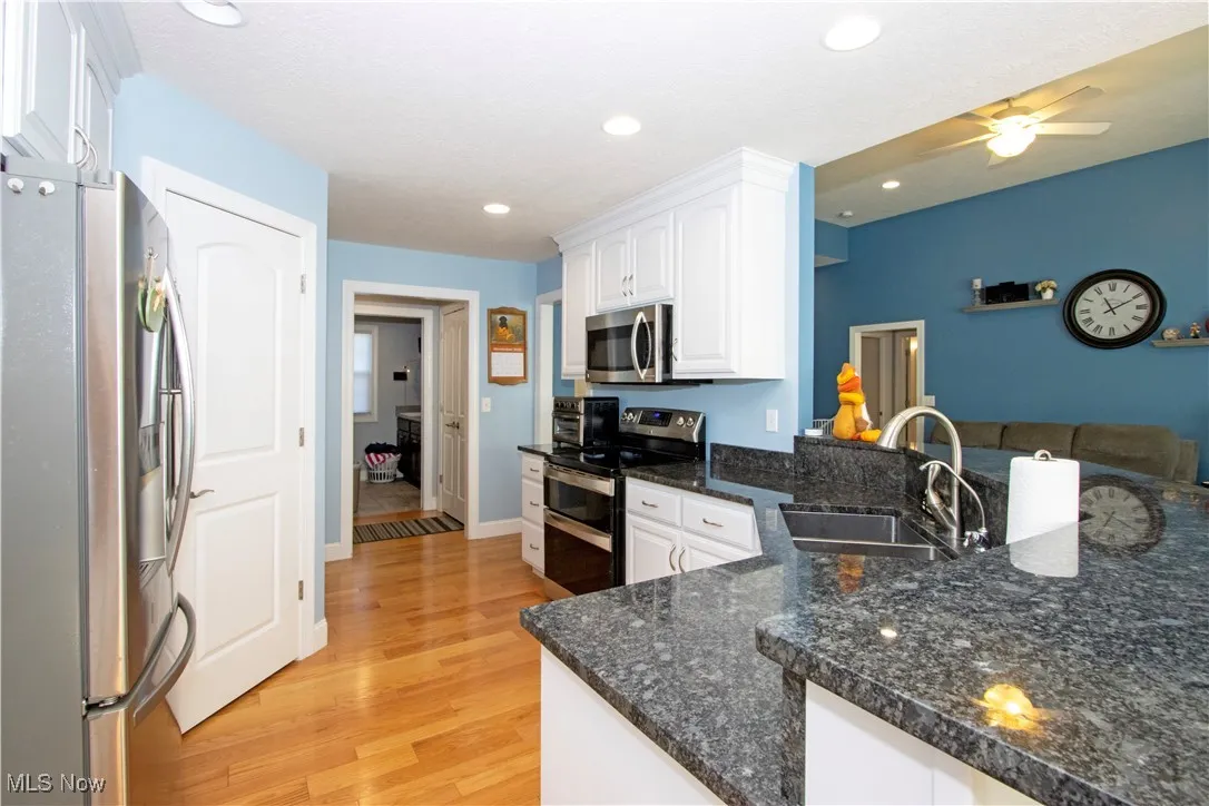 Kitchen with stainless steel appliances, dark stone counters, white cabinetry, light wood-style floors, and recessed lighting