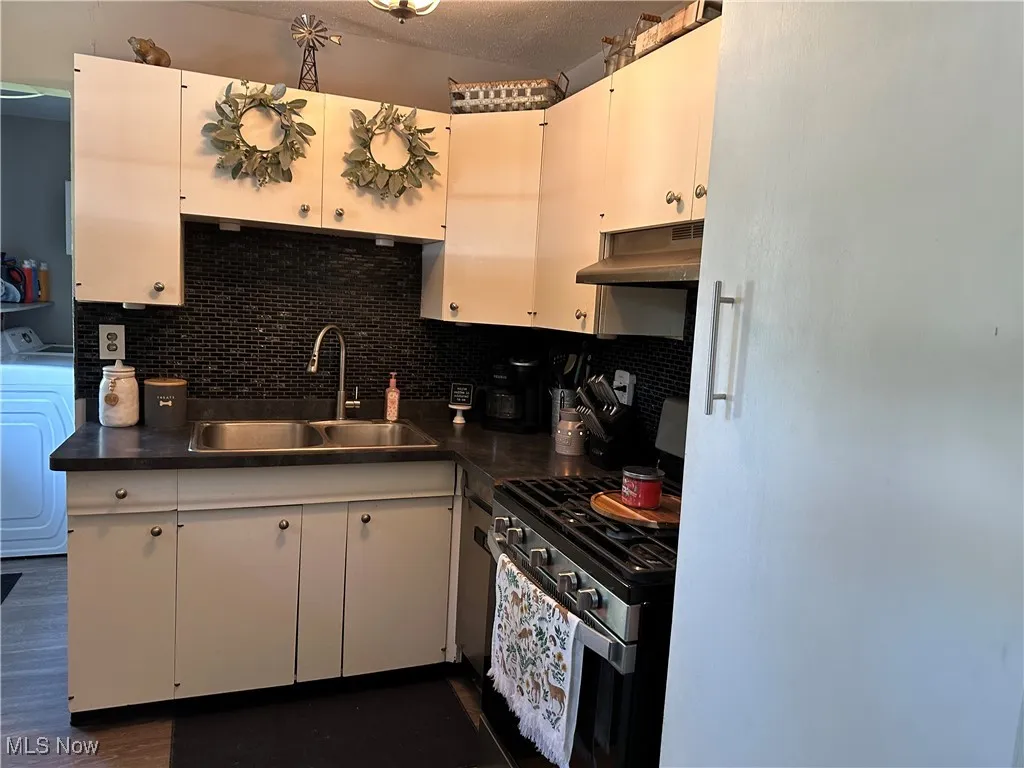 Kitchen with stainless steel gas range oven, tasteful backsplash, under cabinet range hood, dark countertops, and a textured ceiling
