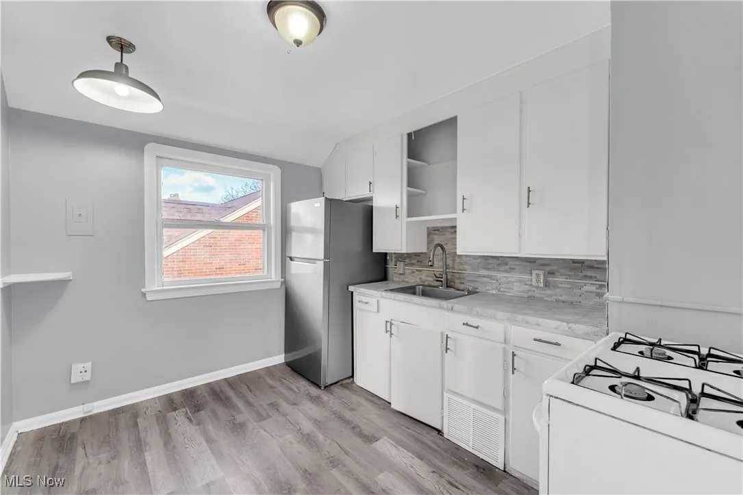 Kitchen featuring open shelves, gas range gas stove, white cabinets, tasteful backsplash, and freestanding refrigerator
