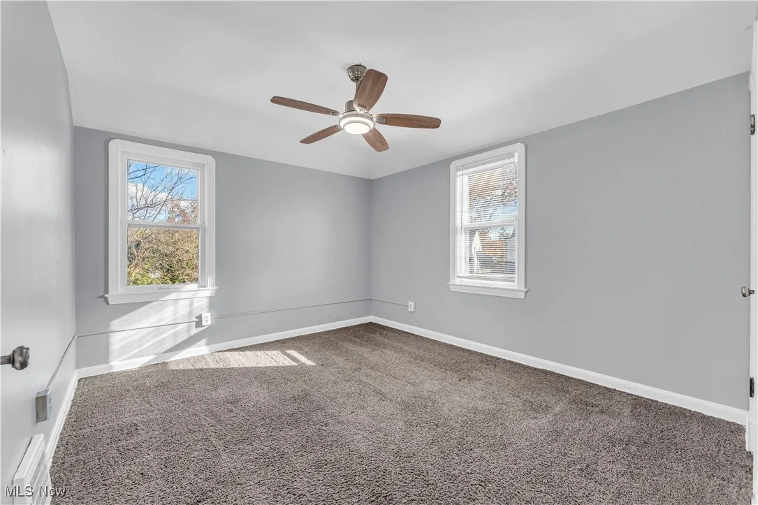 Carpeted empty room featuring a ceiling fan and a baseboard radiator