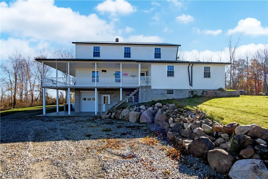 Rear view of house with gravel driveway, an attached garage, a patio, stairway, and a yard