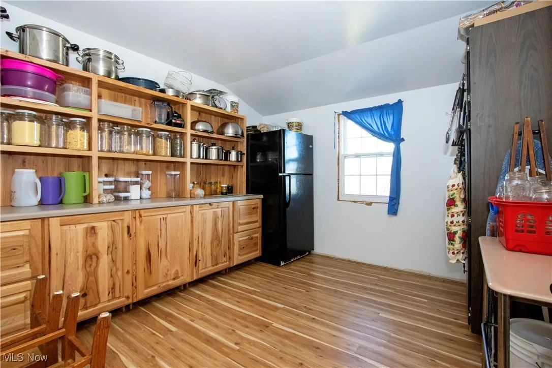 Kitchen with light wood-type flooring, light countertops, lofted ceiling, freestanding refrigerator, and open shelves