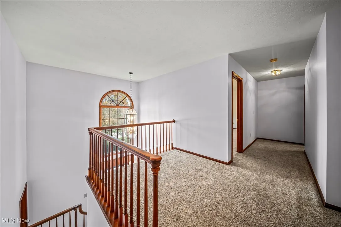 Hall with carpet floors, an upstairs landing, and a chandelier