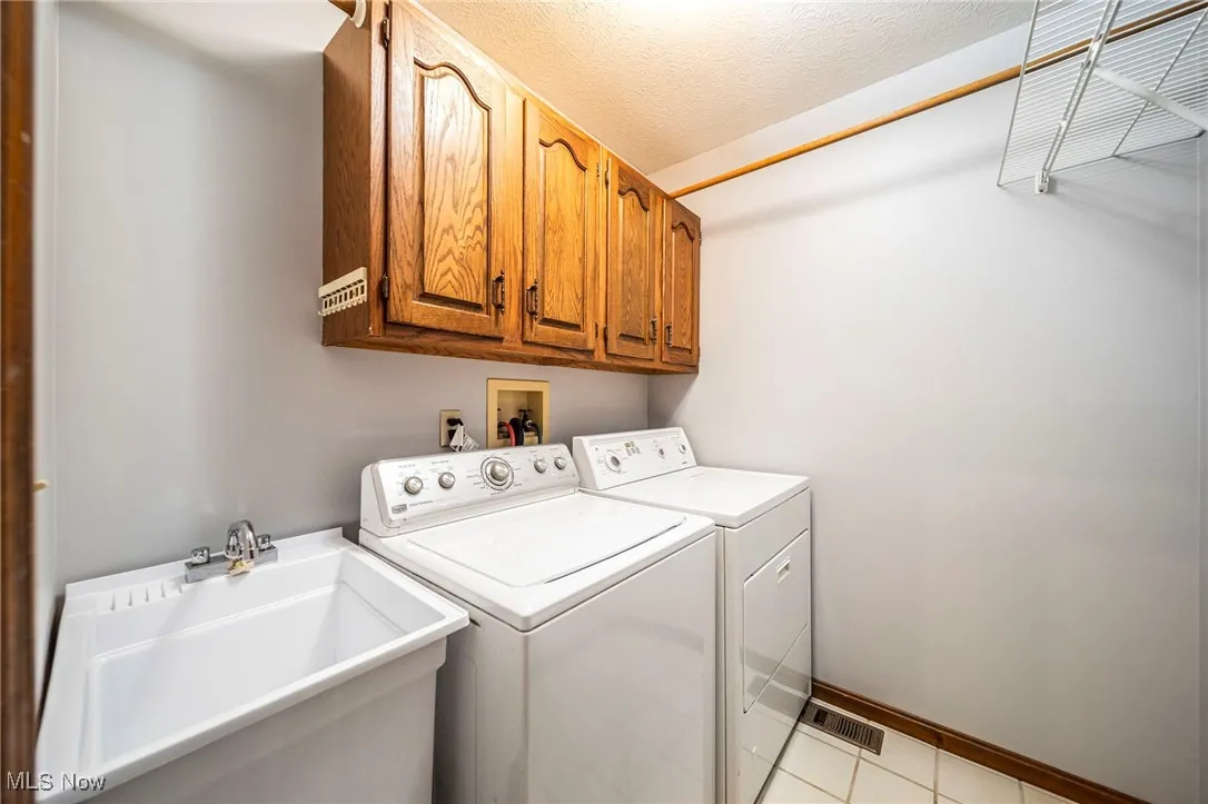 Laundry room featuring washer and clothes dryer, a textured ceiling, light tile patterned flooring, and cabinet space