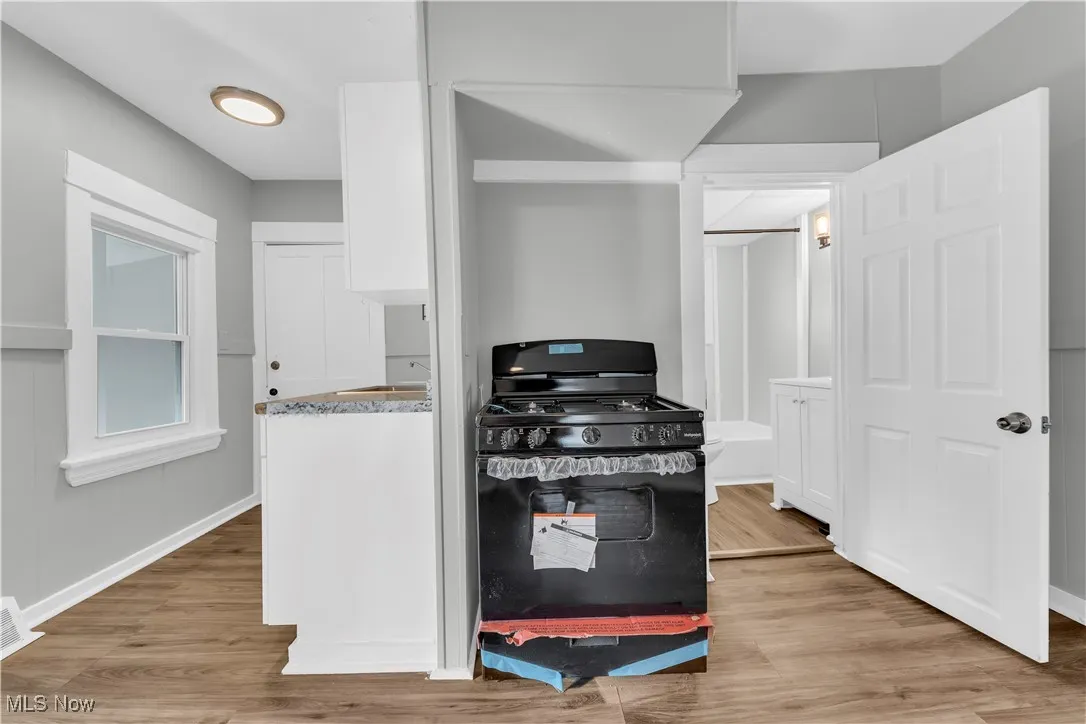 Kitchen featuring black gas range oven, white cabinetry, light wood finished floors, and light stone counters