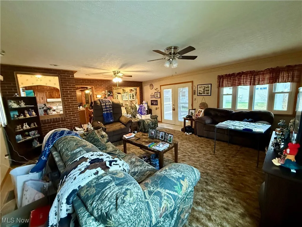Carpeted living area featuring brick wall, a textured ceiling, crown molding, french doors, and ceiling fan