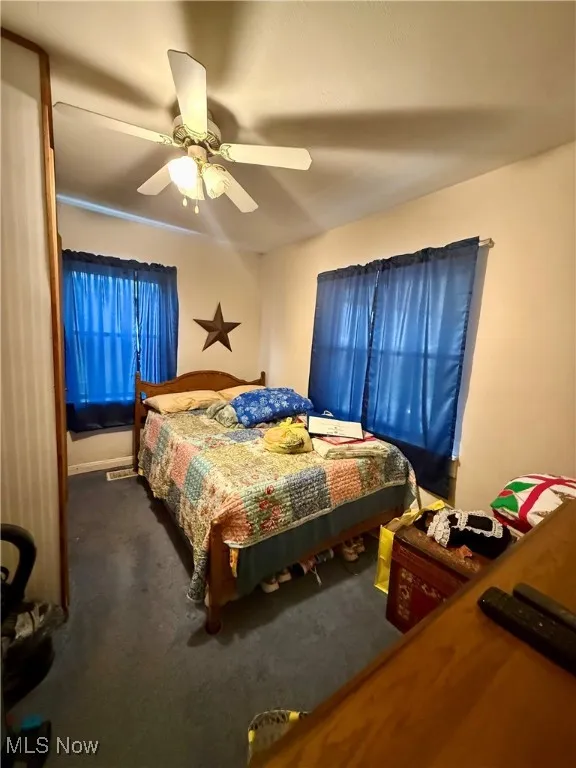 Bedroom with dark colored carpet and a ceiling fan