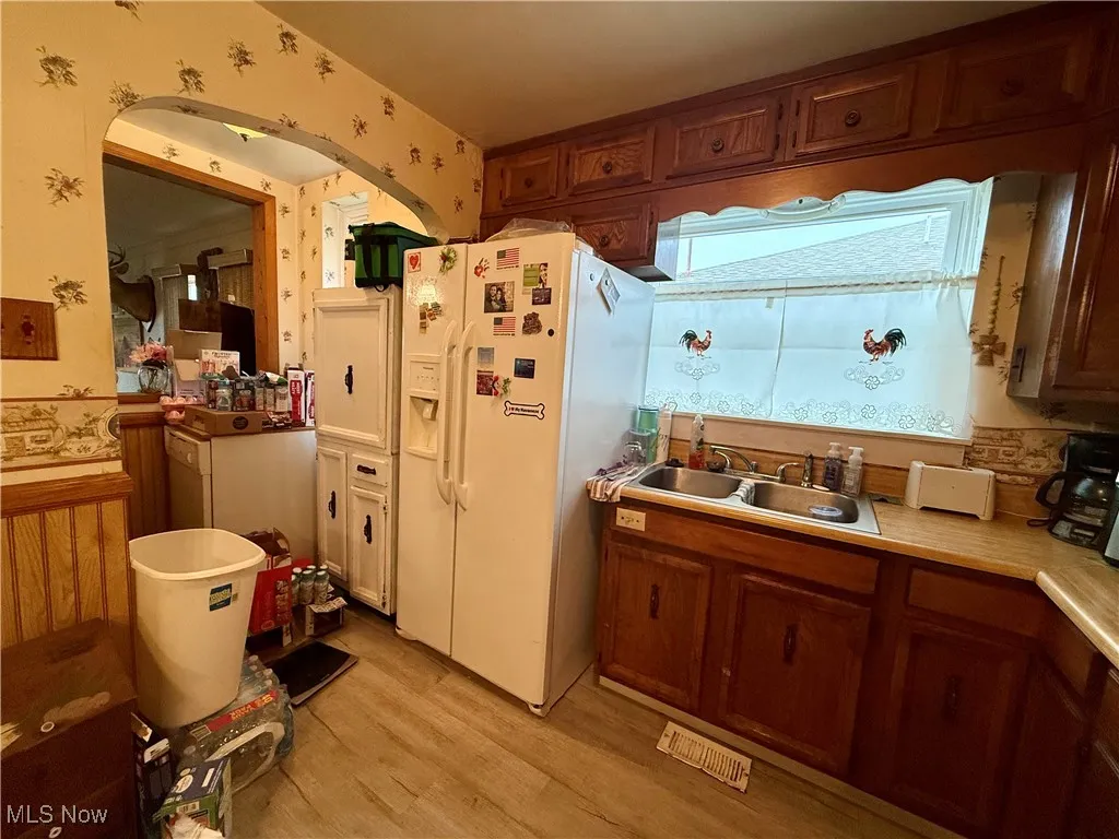 Kitchen with white refrigerator with ice dispenser, light countertops, light wood-style flooring, brown cabinets, and wallpapered walls