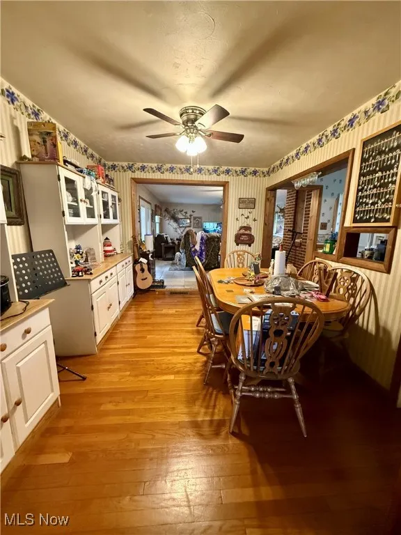 Dining space featuring light wood-style floors, a ceiling fan, and wallpapered walls