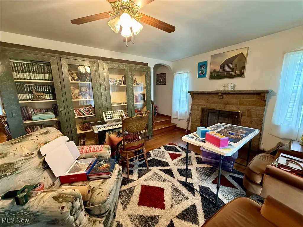 Living area with wood finished floors, a ceiling fan, arched walkways, and a fireplace