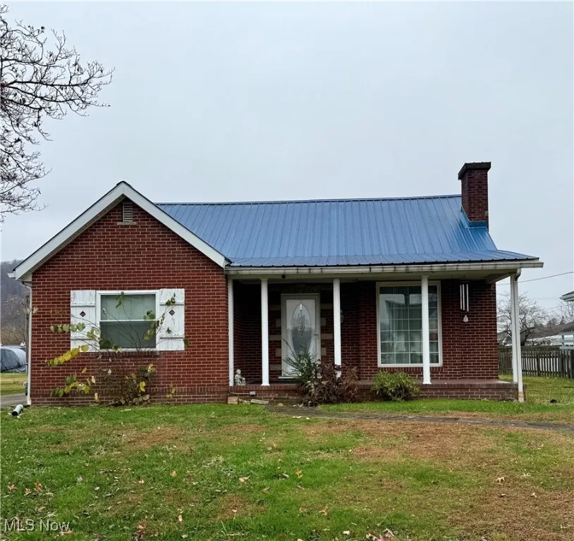 View of front of home featuring a porch, a metal roof, brick siding, a front yard, and a chimney