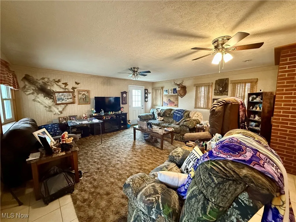 Living area featuring ornamental molding, a textured ceiling, light tile patterned floors, and a ceiling fan