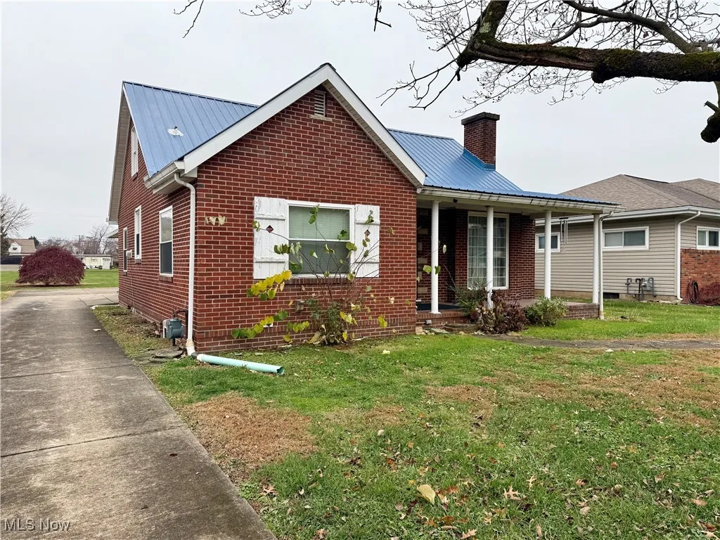 View of front facade featuring a front yard, a chimney, covered porch, and brick siding